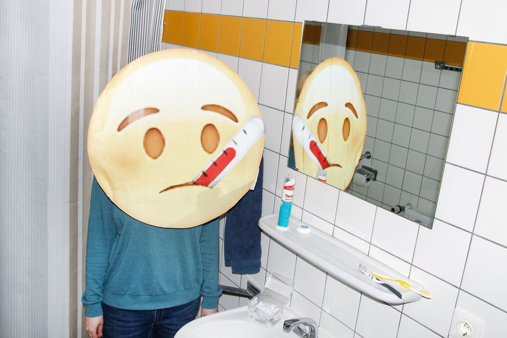 Emoji mit Fieberthermometer im Mund steht vor dem Badezimmerspiegel (Foto: Renke Brandt)