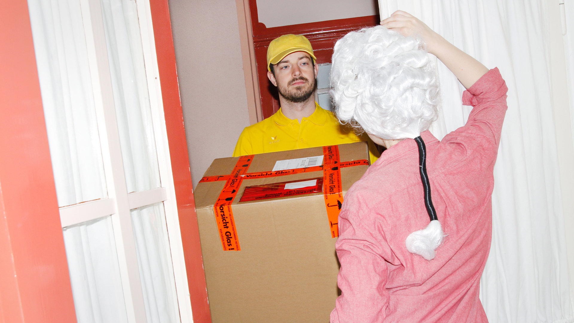 Frau mit Mozart-Perücke nimmt an der Haustür ein Paket an (Foto: Renke Brandt)