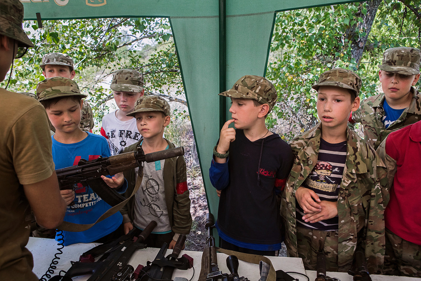 Kinder in Militärkleidung begutachten eine Kalaschnikow