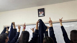 Viele junge Frauen halten einem Foto eines iranischen Politikers den Mittelfinger entgegen