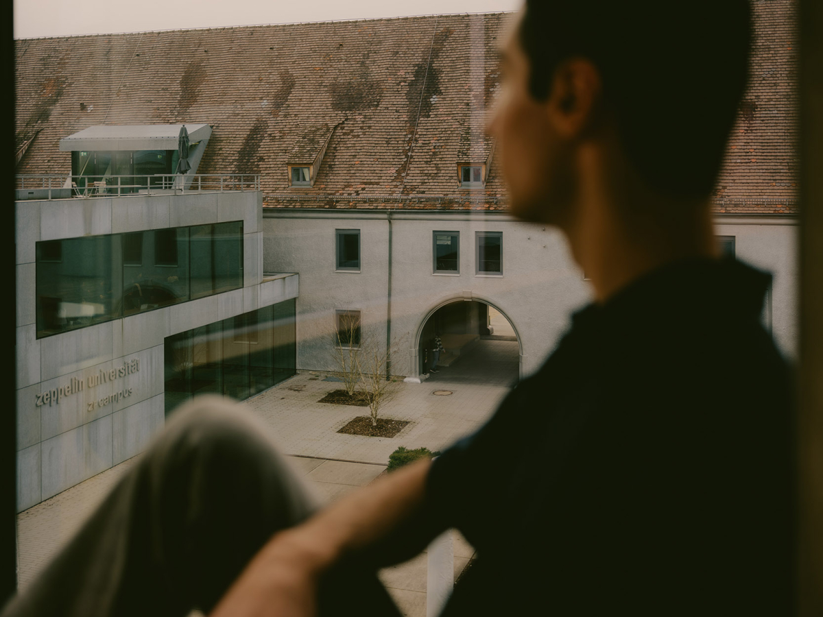 Ferhat sitzt auf der Fensterbank und blickt auf den Campus der Uni Ferhat sitzt auf der Fensterbank und blickt auf den Campus der Uni
