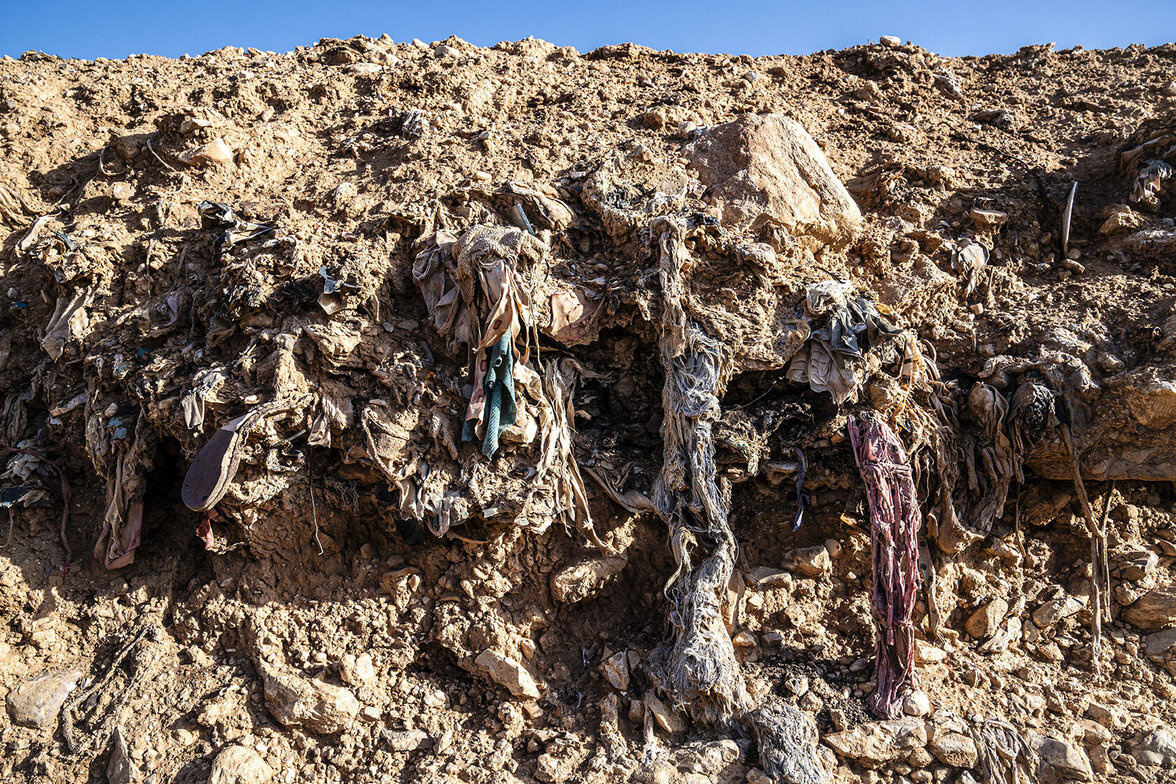 Knochen und Kleidungsstücke in den Erdschichten eines Massengrabs Knochen und Kleidungsstücke in den Erdschichten eines Massengrabs
