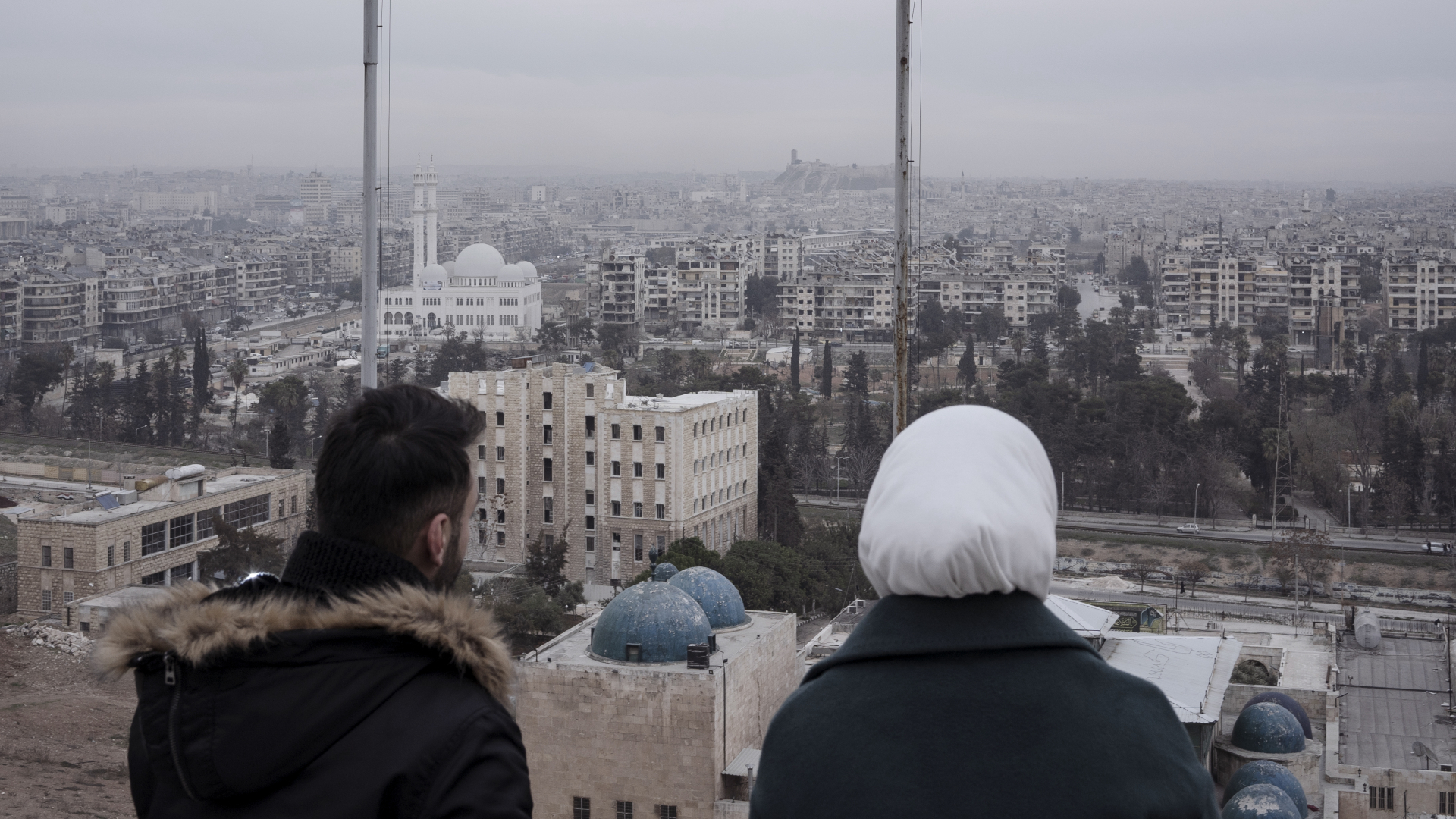 Zwei Menschen blicken von einem Berg auf Aleppo
