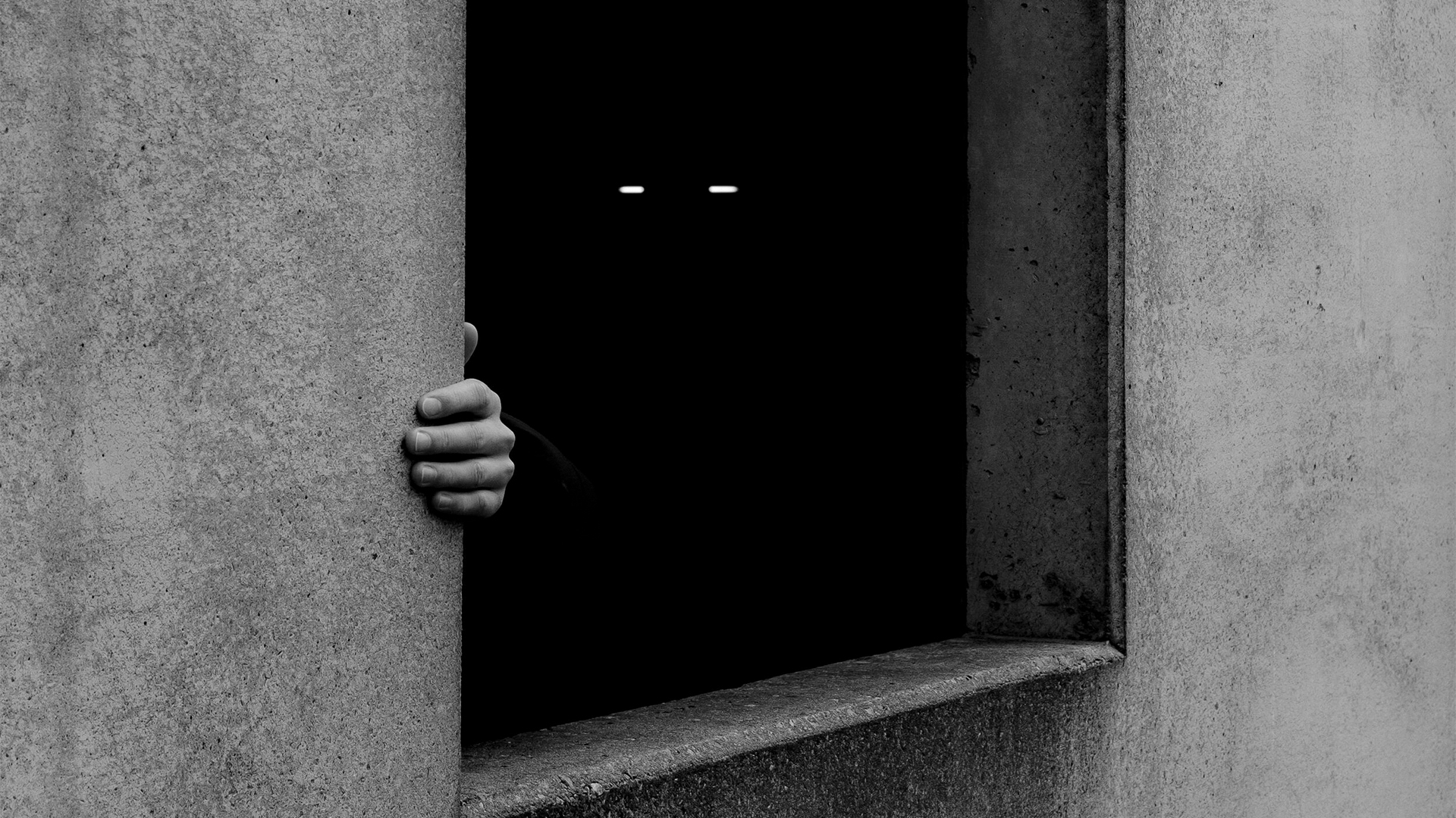 Hand und leuchtende Augen in einem dunklen Fenster