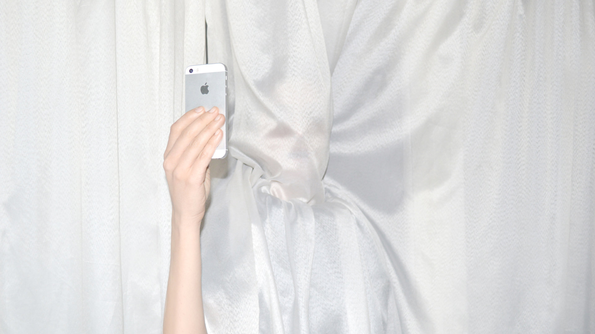 Frau mit iPhone hinter einem Vorhang