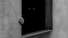 Hand und leuchtende Augen in einem dunklen Fenster