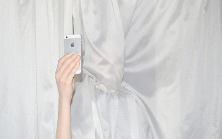 Frau mit iPhone hinter einem Vorhang 