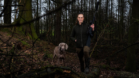 Fee Brauwers steht im Wald in Jagdkleidung, neben ihr ein Hund
