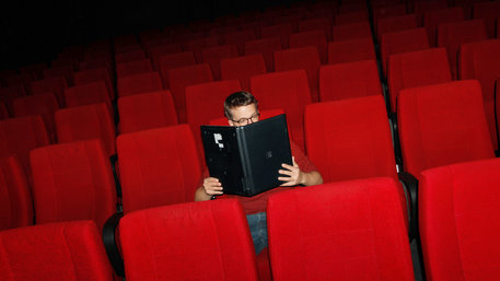 Ein Mann sitzt in einem Kinositz und liest im Laptop