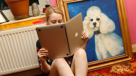 Junge Frau hält einen Laptop wie ein Buch, als würde sie darin lesen