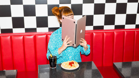 Frau sitzt im American Diner und liest in einem laptop