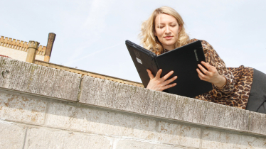 Mann sitzt auf Balkon und liest in einem Laptop Eine Frau liest in einem Laptop