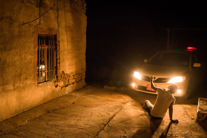 Im Scheinwerferlicht eines Autos sitzt ein junger Mann telefonierend am Boden  (Foto: Chris Grodotzki)